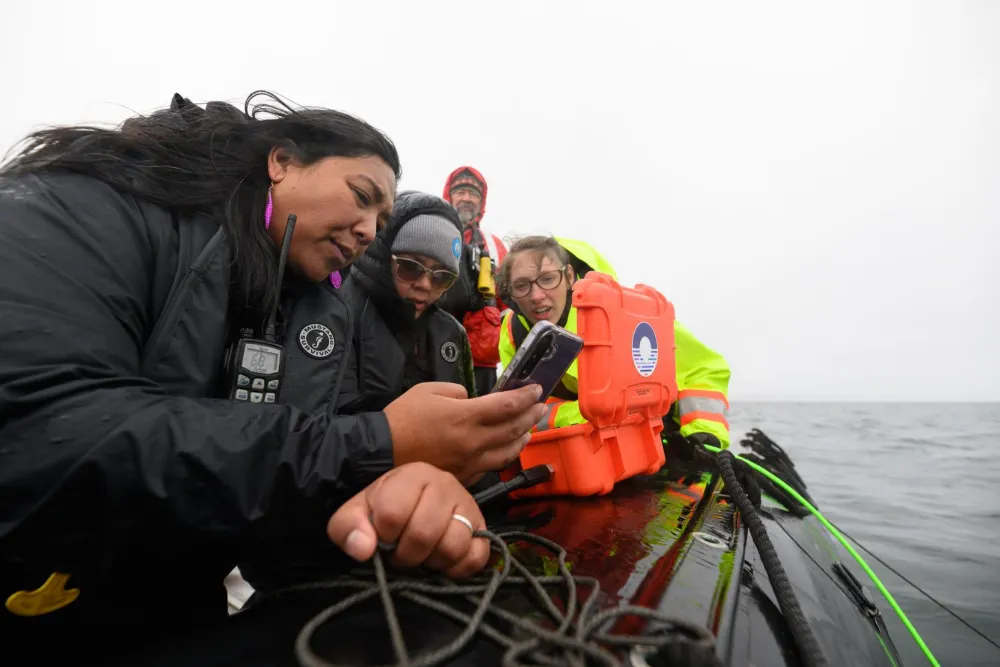 People on a boat gathered around equipment and looking at a phone