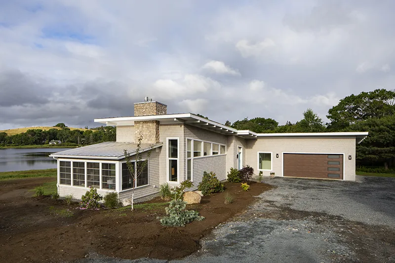 A beige house with a garage and lots of windows built on the lakeshore