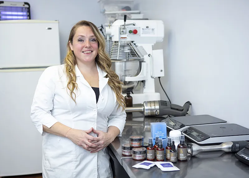 A woman standing next to a counter with Sohma Naturals products on it