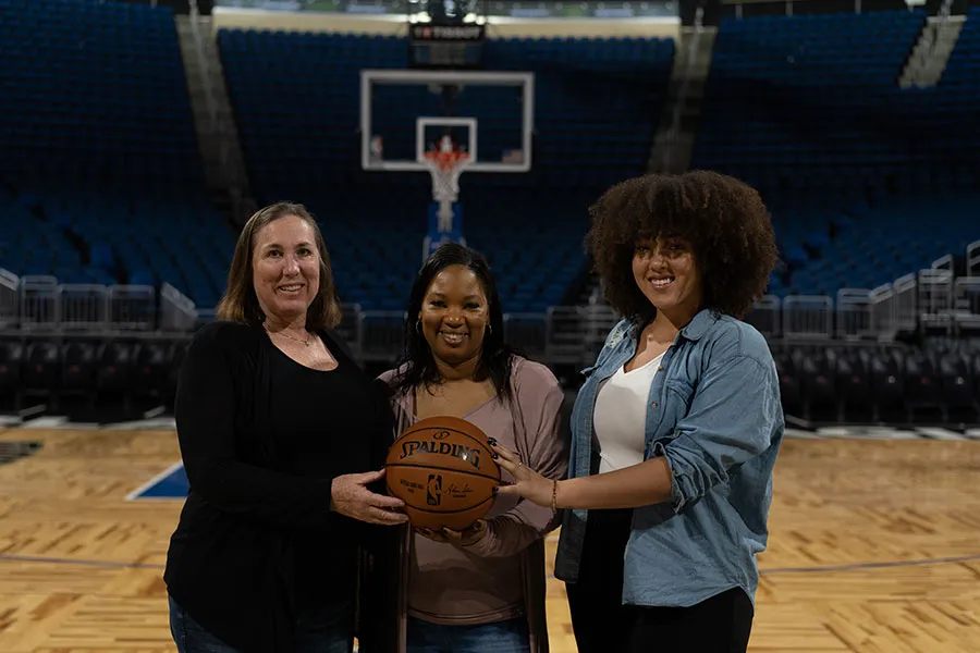 Three hosts of the Court-Side Moms podcast stand jointly holding a basketball