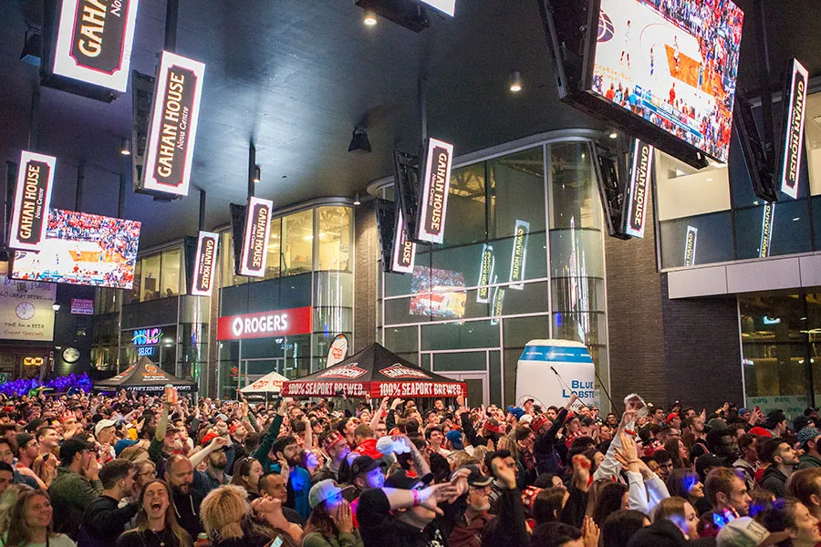 Wide shot of crowd standing outside looking up at screens that are showing a Toronto Raptors basketball game