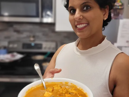 Woman holding a bowl of Indian food in a kitchen
