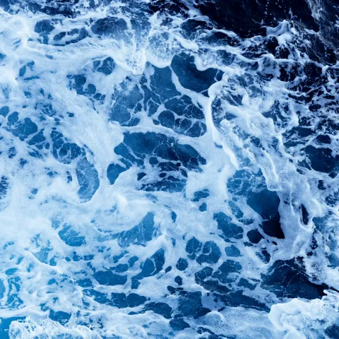 Deep blue ocean water with turbulent waves forming white foam and moving currents