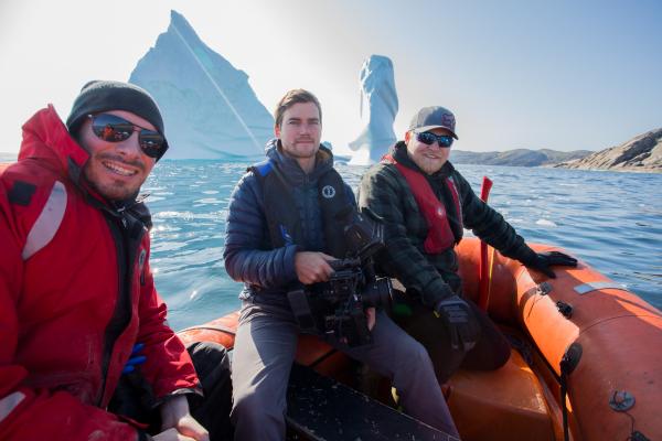People on board a ship pose for a photo with an iceberg in the background