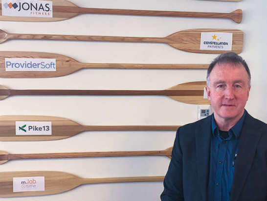 Jonas Software Operations Manager, Tim Richardson, stands in front of a display showing various Jonas brands.